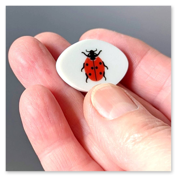 Handgefertigter Schmuck aus einer Porzellanscherbe. Marienkäfer auf weißem Hintergrund.